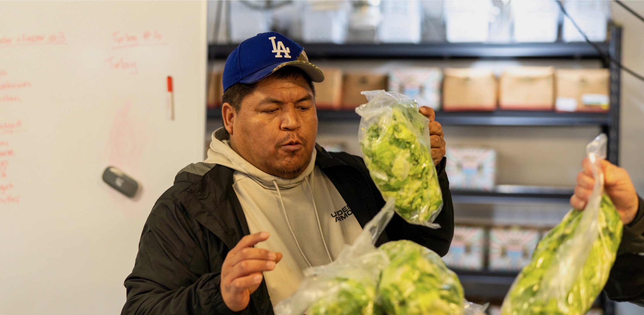 Man with cap and jacket holding bag of greens at store.