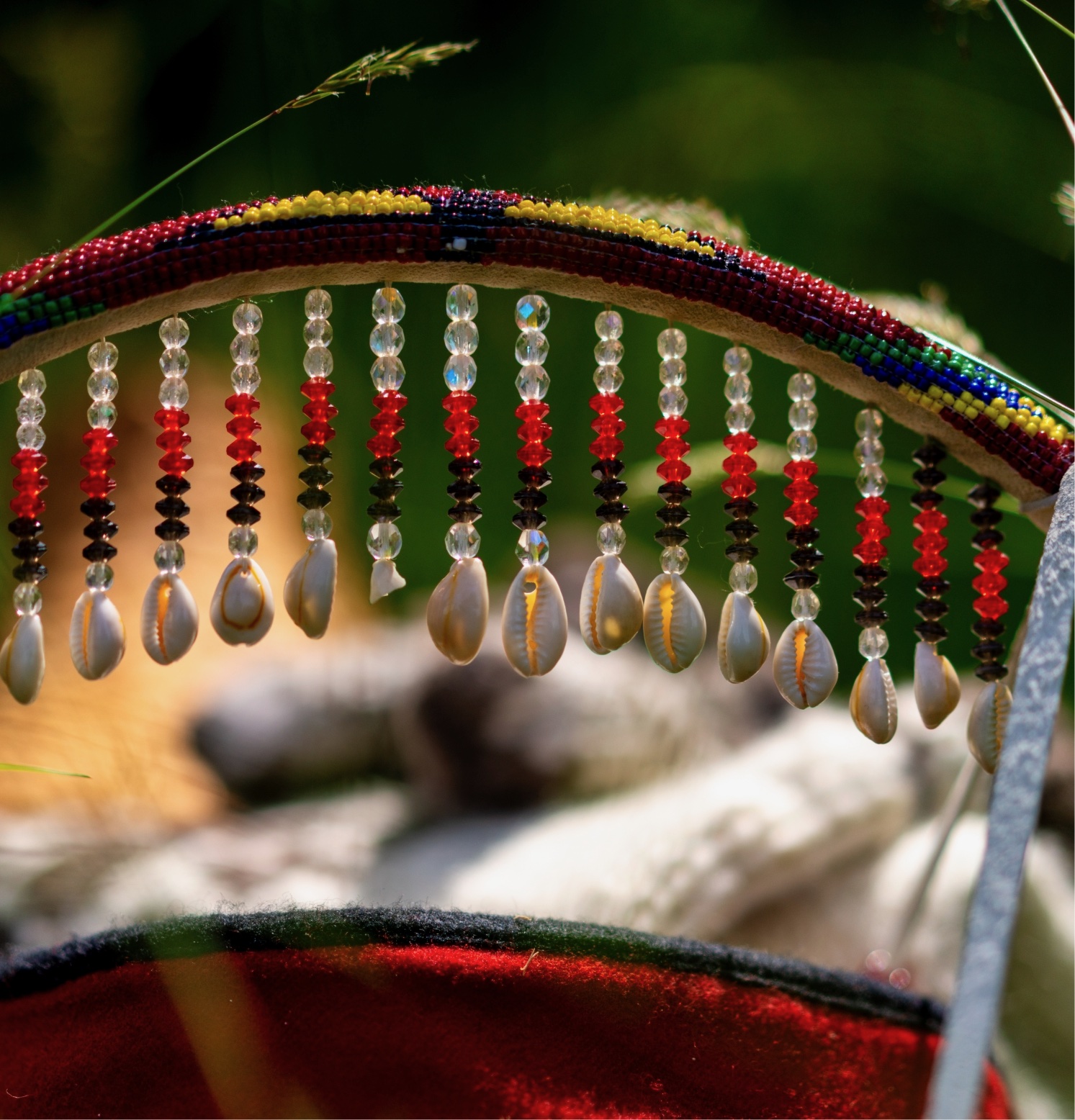 A colorful beaded necklace with beads and a string of pearls is hanging from an object against a blurred background.
