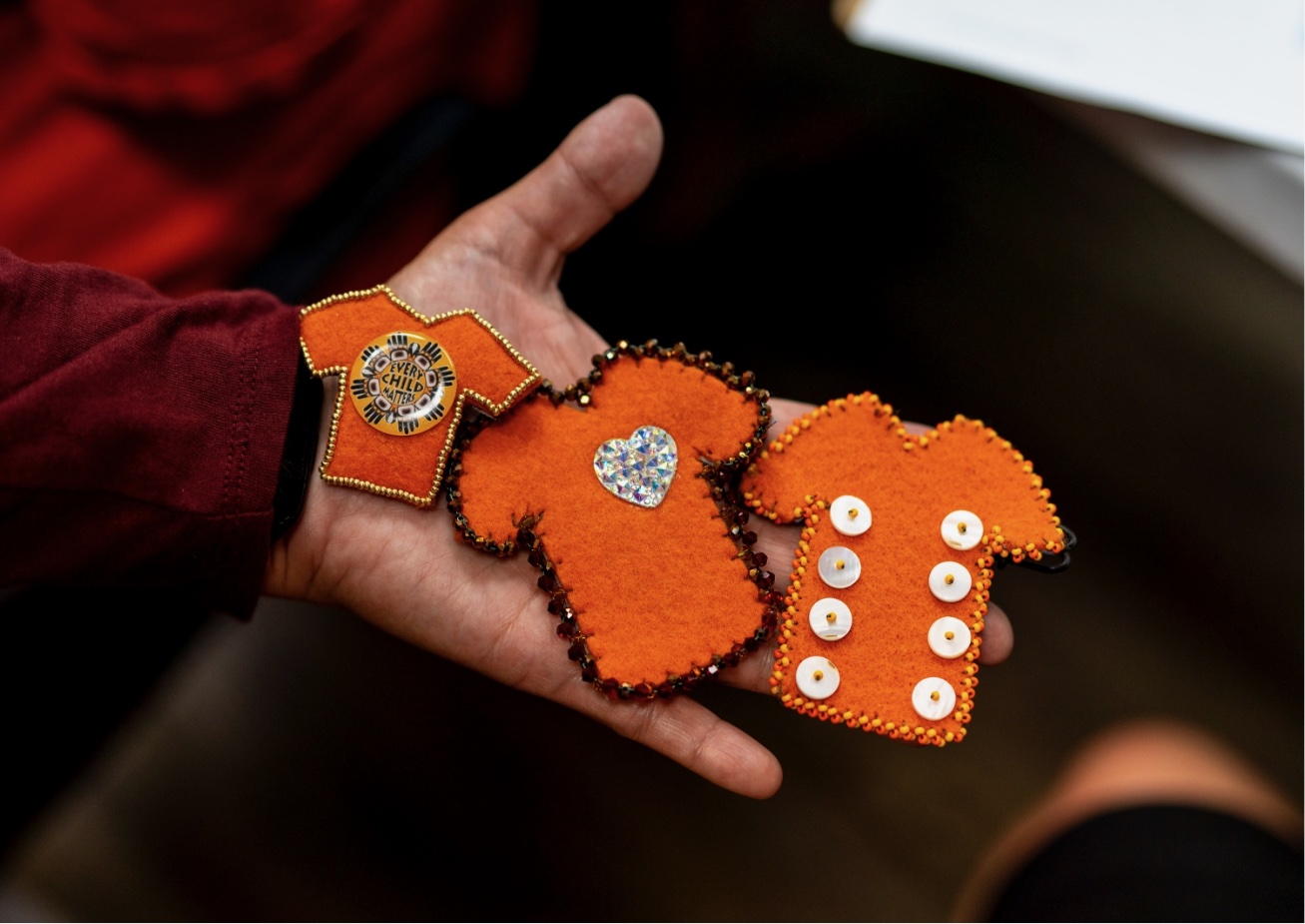 A hand holds two orange fabric toys with buttons and a wristwatch.