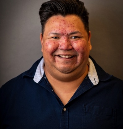 Man with dark hair and dark shirt against grey background.