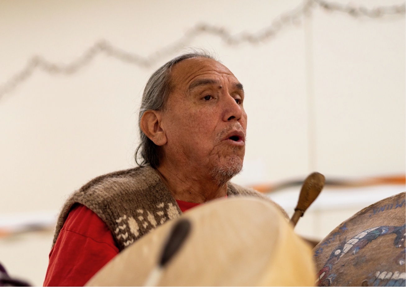 An old man with a beard is speaking into an instrument while wearing traditional clothing.