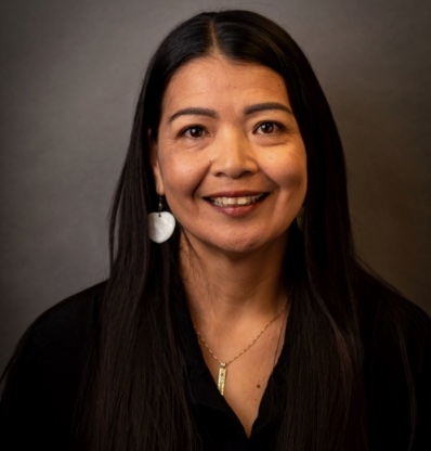 A person with long hair and a necklace is smiling.