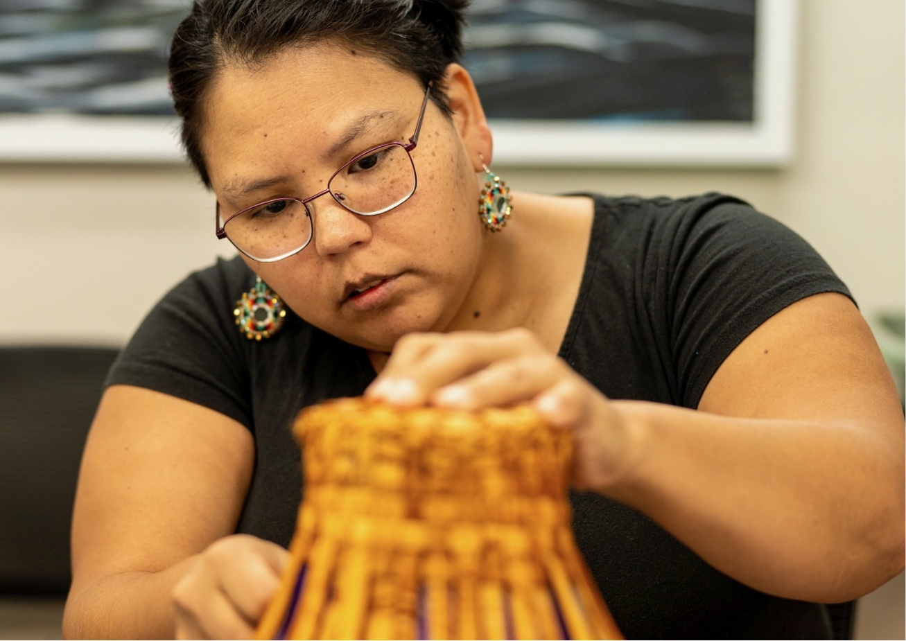 A person is holding a yellow object with blue designs while wearing glasses and earrings.