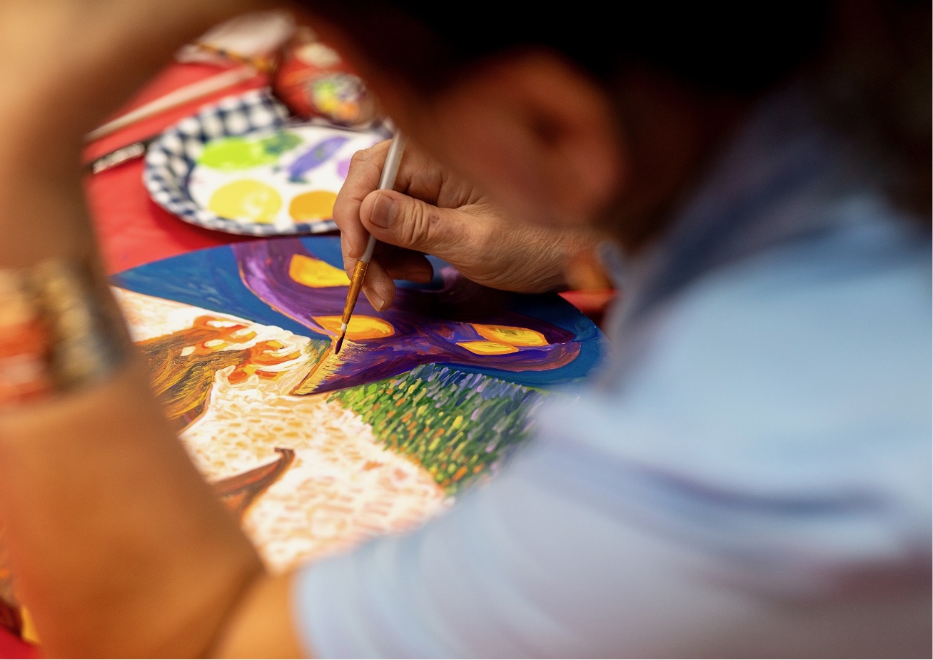 Person painting with paintbrush and palette knife at table.