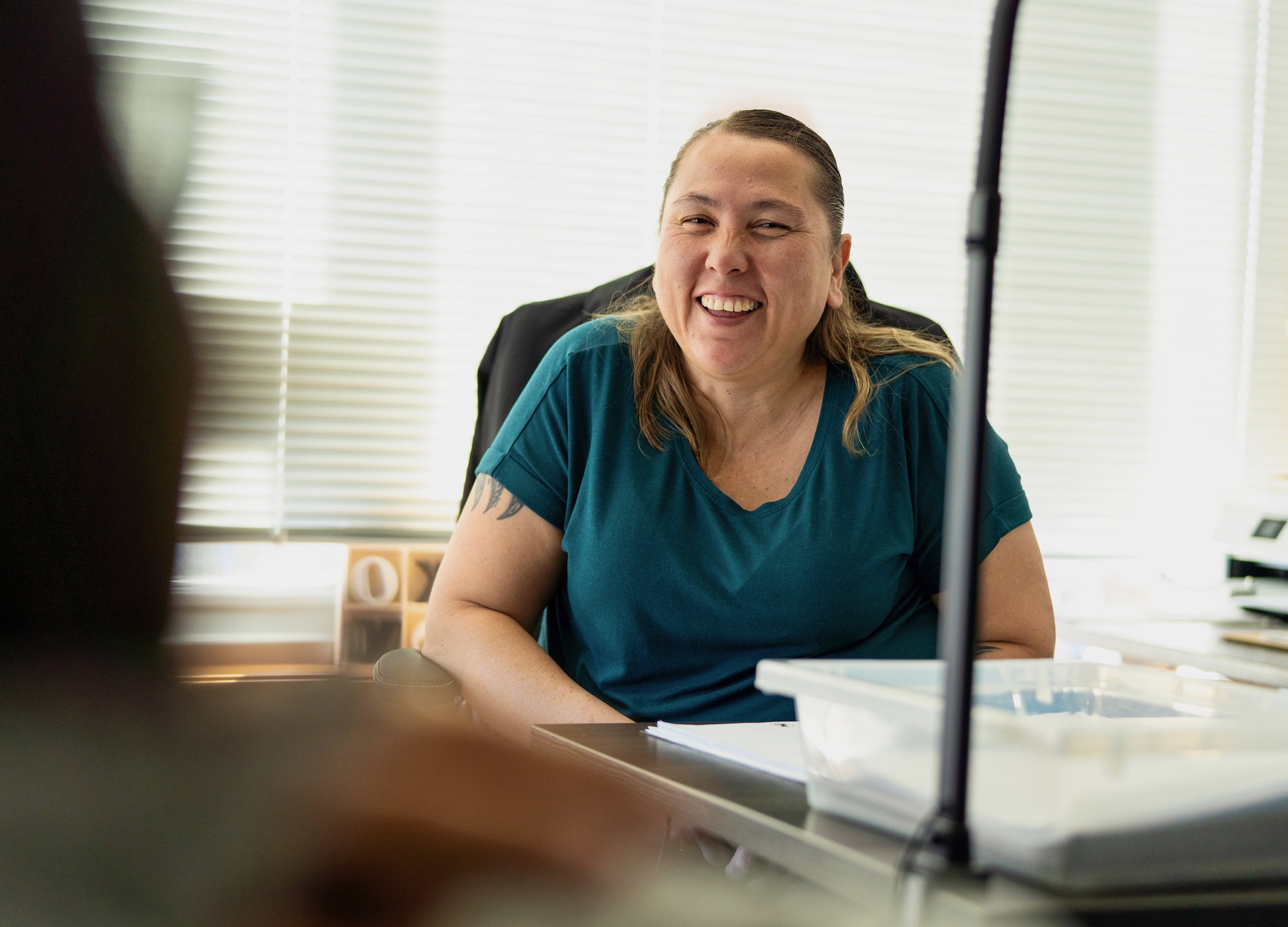 A person is sitting at a desk with papers and smiling.