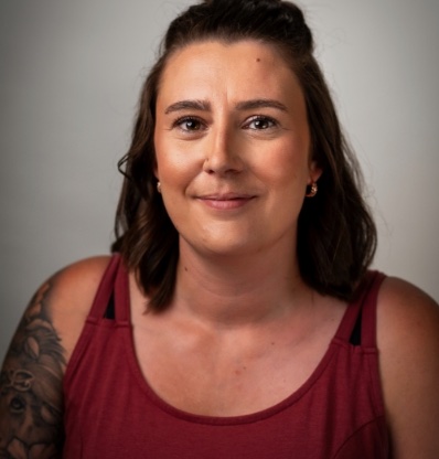 A person with a tattoo is wearing a red tank top and has long hair.