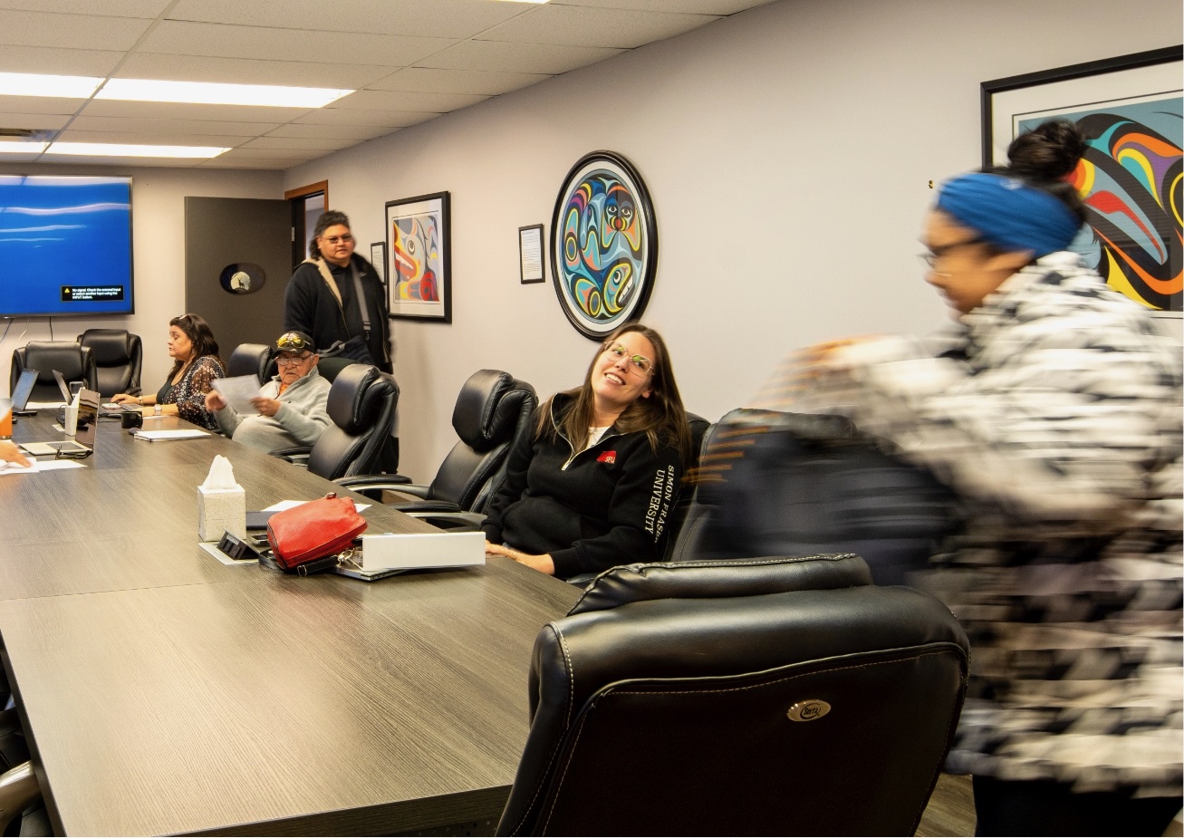 A blurry photo of people sitting at a table with various objects and artwork on walls.