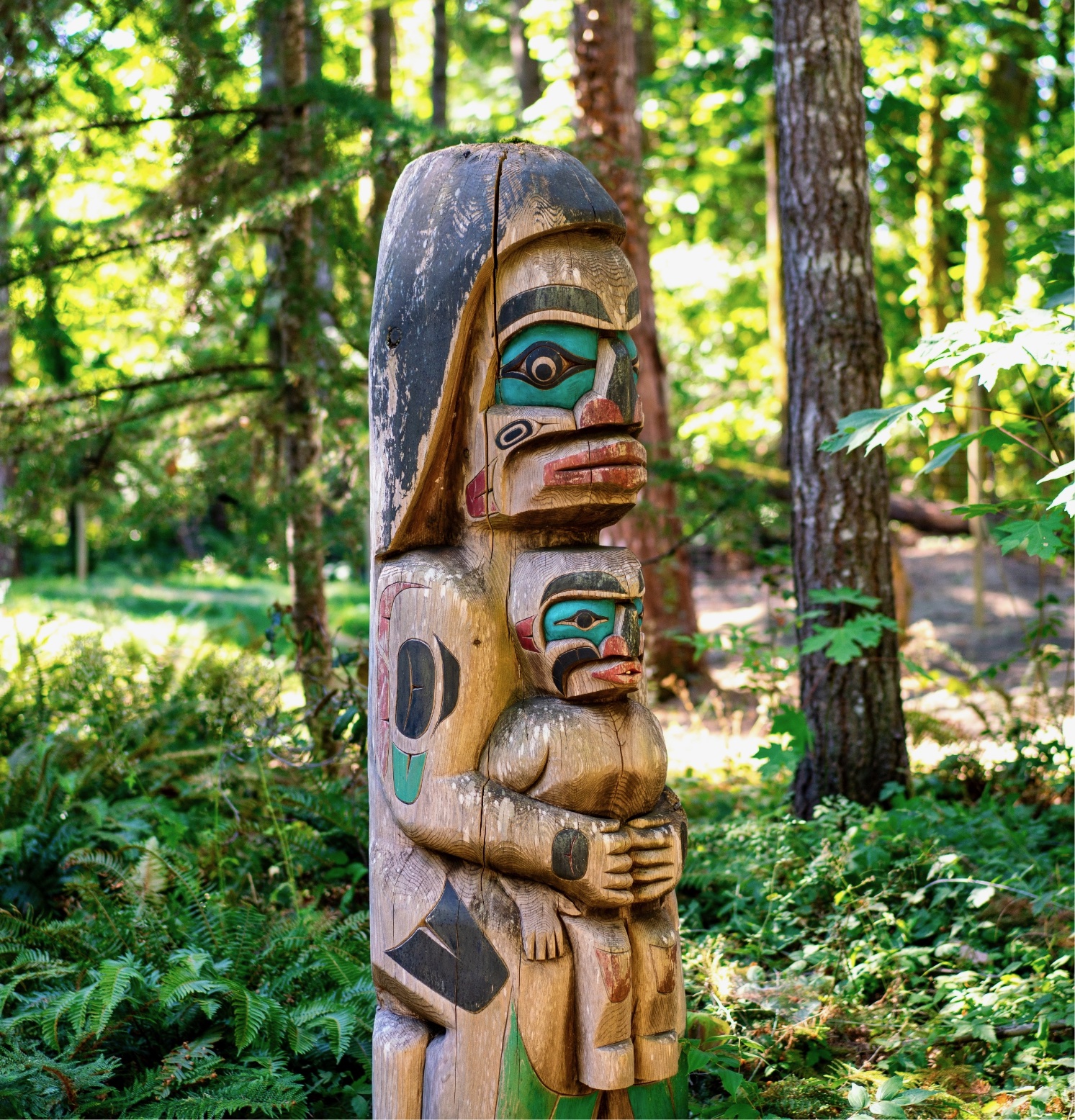 A wooden totem pole with a face carved into it stands amidst trees and foliage.
