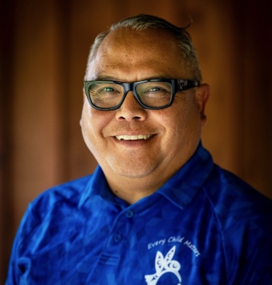 Man wearing glasses and blue shirt with logo smiling.