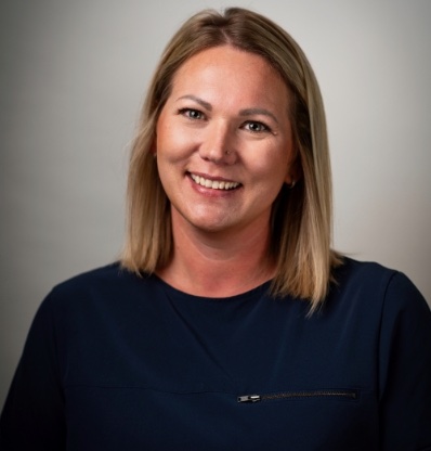 A woman with blonde hair and a dark blue shirt is smiling at the camera.