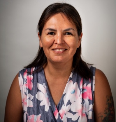 A woman with a floral shirt is smiling against a plain background.