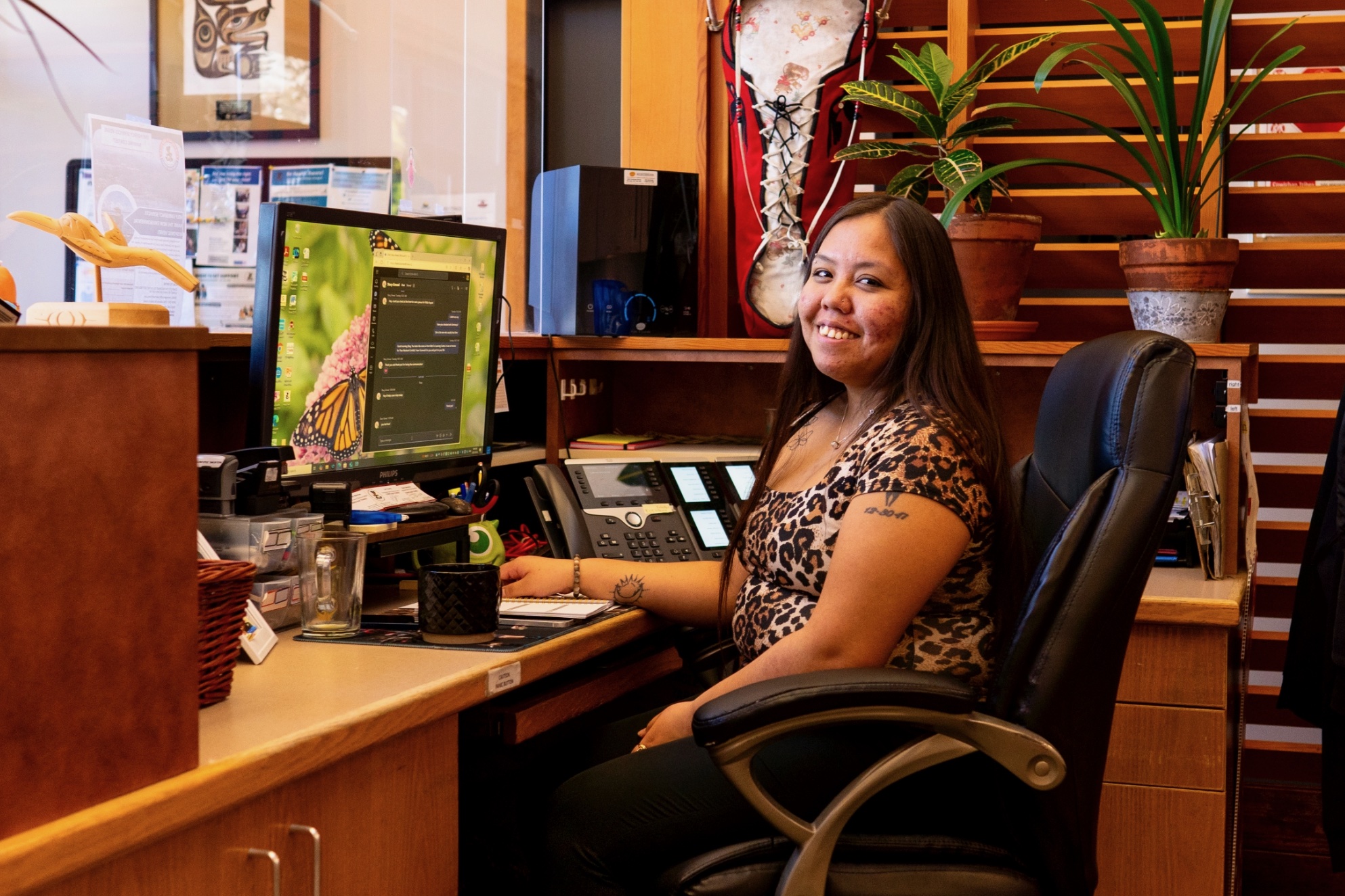 A woman is sitting at a desk with her hand on it and smiling while working on a computer.