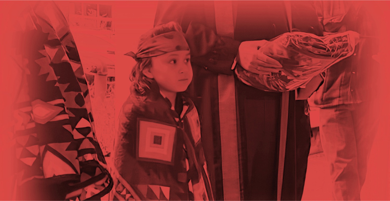 A person with a patterned headscarf and bag is standing next to another object.