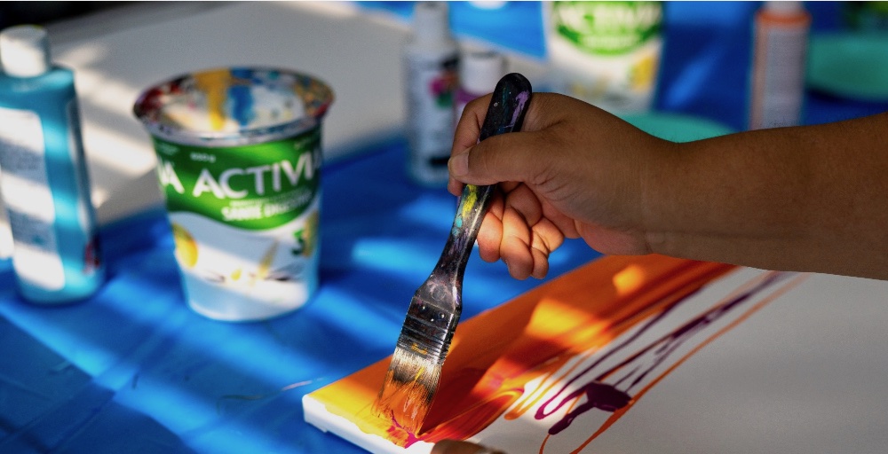 A hand holding a paintbrush over an orange and yellow painting with 'ACTIVA' written on it.