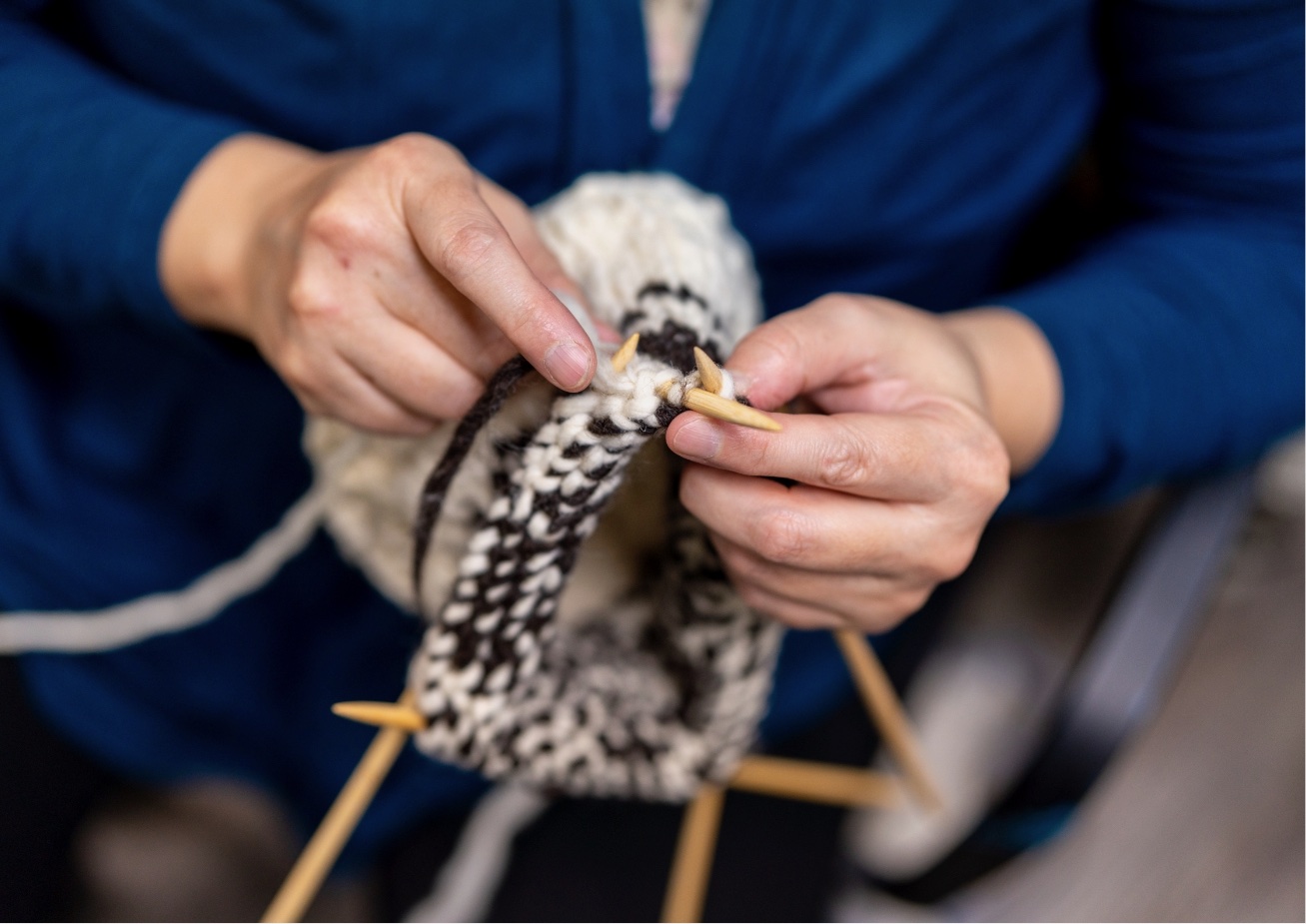 A person is knitting with a white and black yarn while wearing blue clothing.