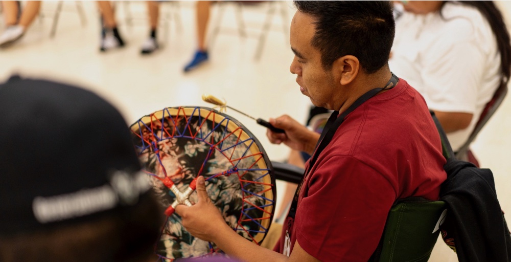 A person is playing a traditional musical instrument with colorful strings and beads.