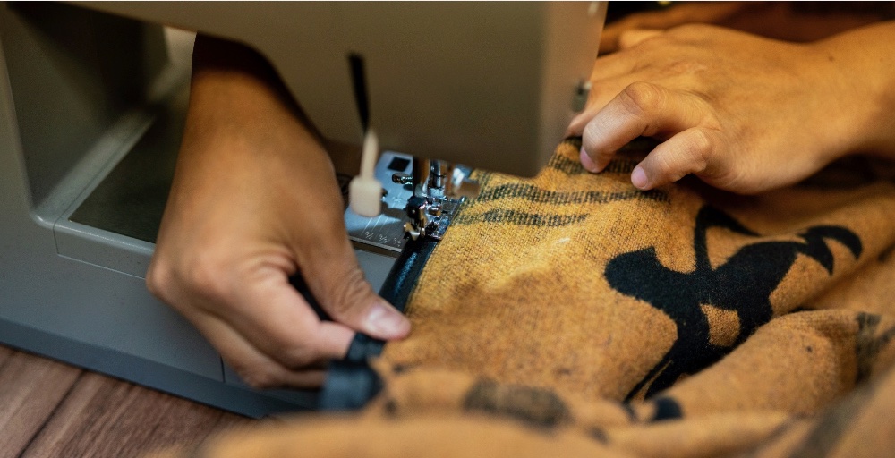 A person is sewing a brown shirt with black designs on it.
